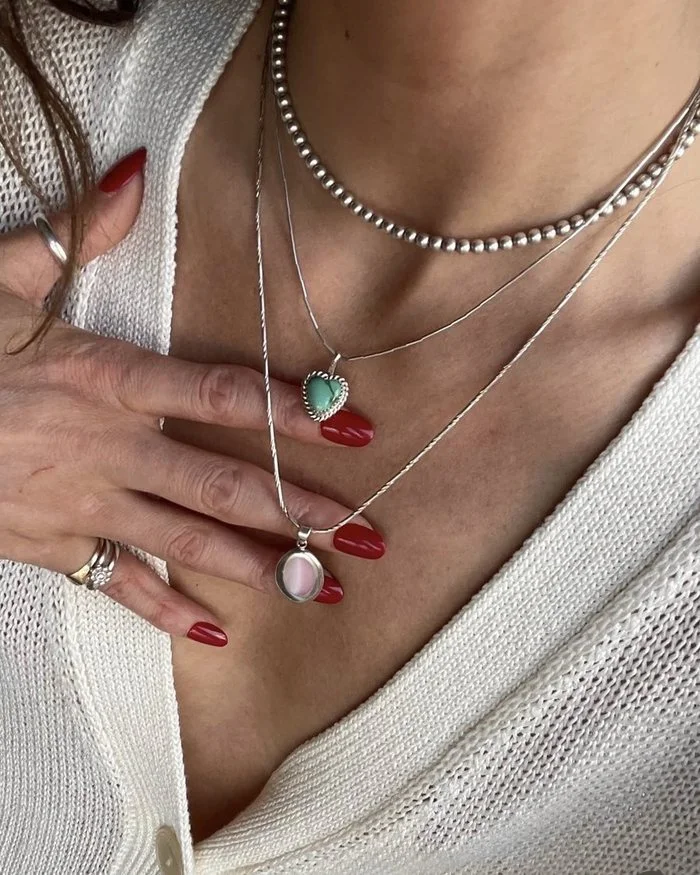 Anita wearing layered vintage sterling silver necklaces with a turquoise heart pendant and a pink shell pendant